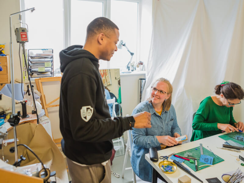 A woman smiling up at the teacher, who is teaching her jewellery making