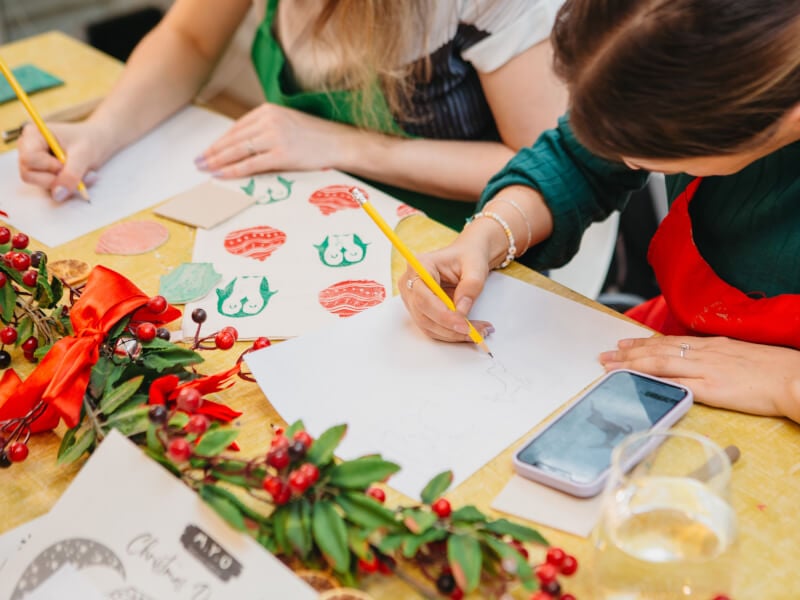 Woman drawing on paper with pencil surrounded by Christmas decorations