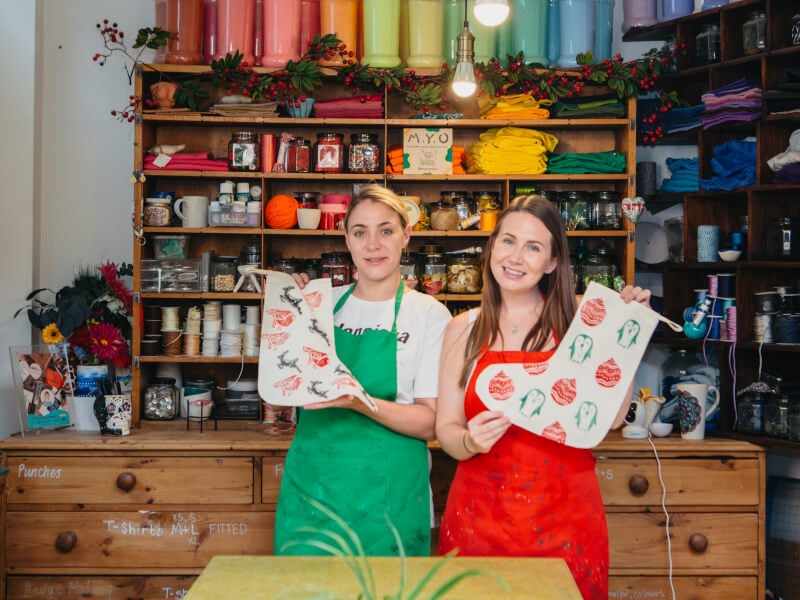 Two women in red aprons holding handmade stockings