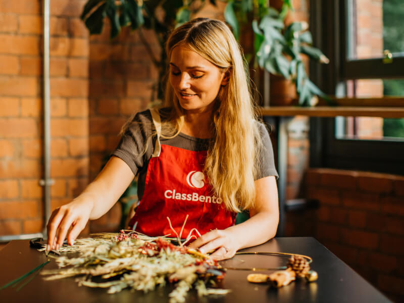 Woman wearing apron smiling whilst making a DIY Christmas wreath. 