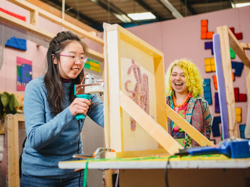 Two friends laughing while attending a tufting class