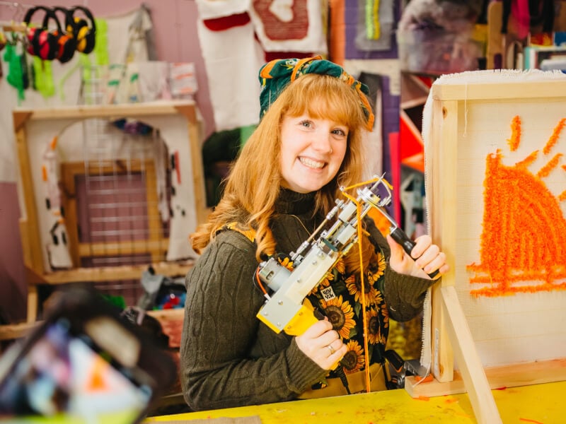 A woman holding a tufting gun and smiling 