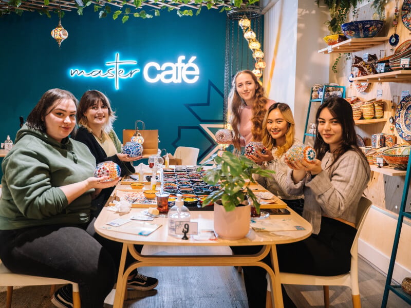 Women smiling sat around a table holding Turkish mosaic lamps.