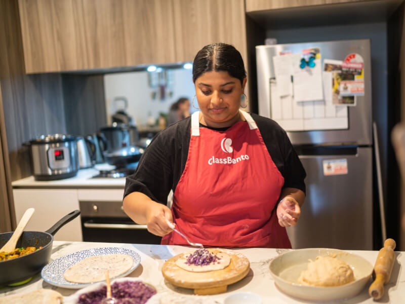 A woman in a ClassBento apron learning how to cook Indian food