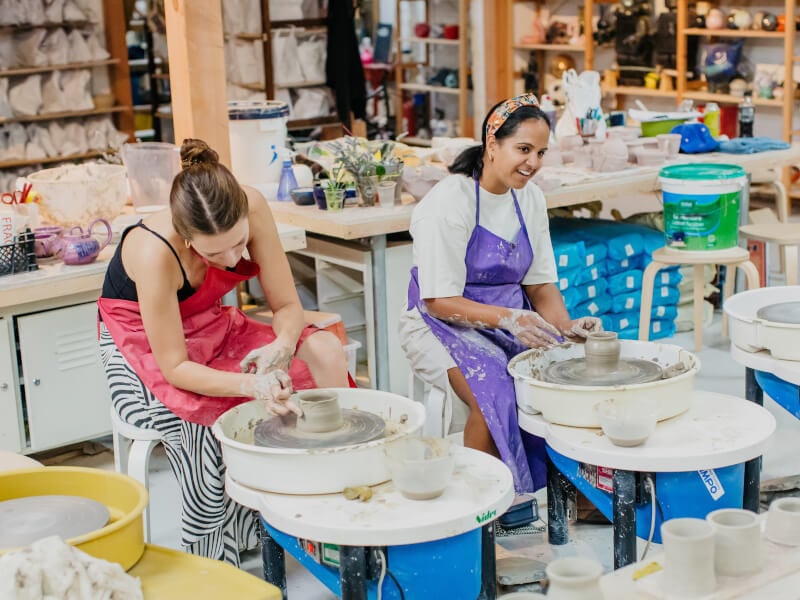 Two women sitting behind pottery wheels in a ceramics studio