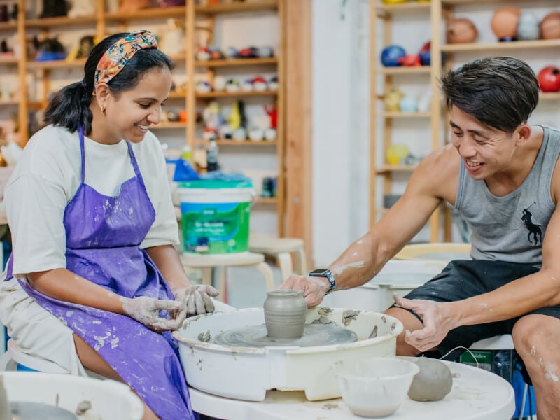 A man and a woman enjoying a wheel throwing class