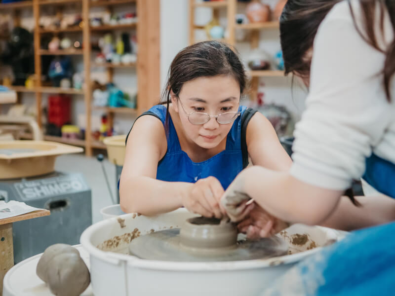 Woman helping another woman on a pottery wheel