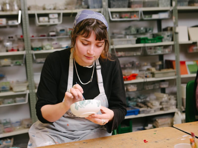 Young woman in an apron painting a ceramic bowl