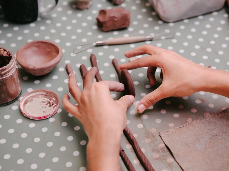 Hands rolling up a long piece of clay into a coil shape