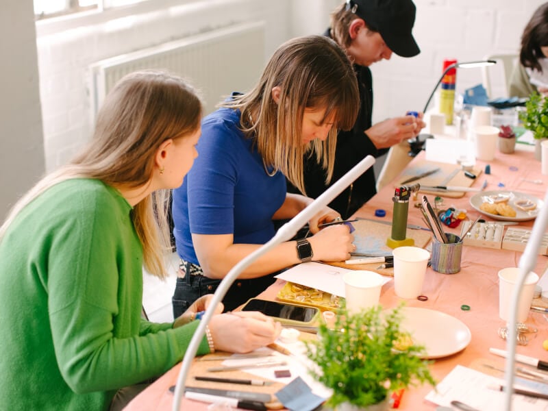 Two women and a man seated at a silversmithing class