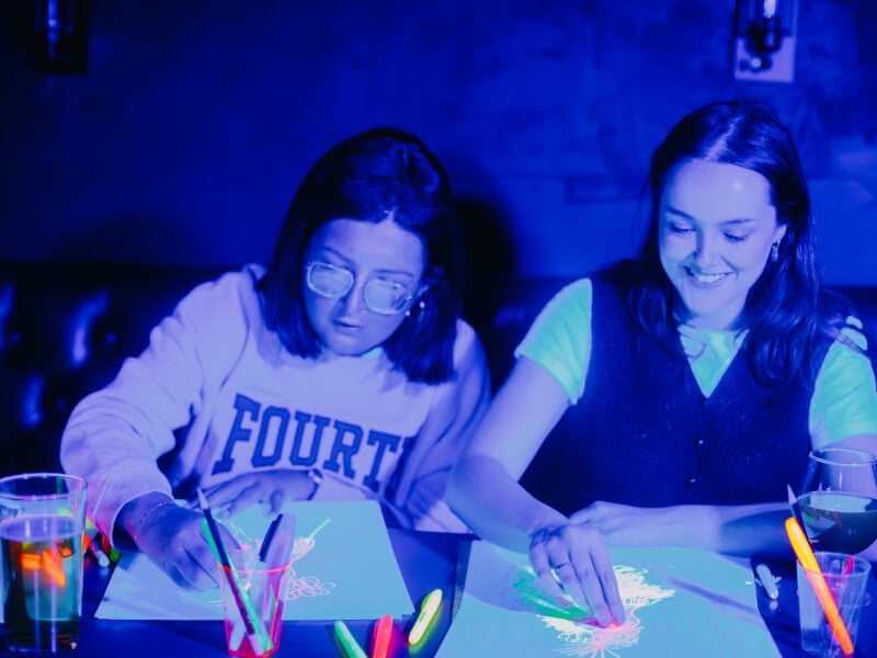 Two women painting under UV light