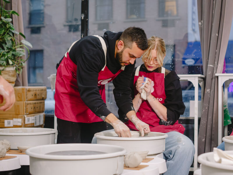 A man helping a woman at a wheel throwing class