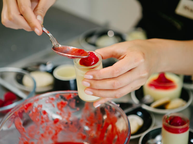 Hand spooning berry coulis onto a panna cotta