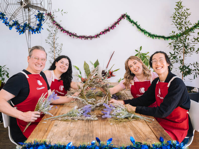 A group of people wearing aprons holding a DIY Christmas wreath. 