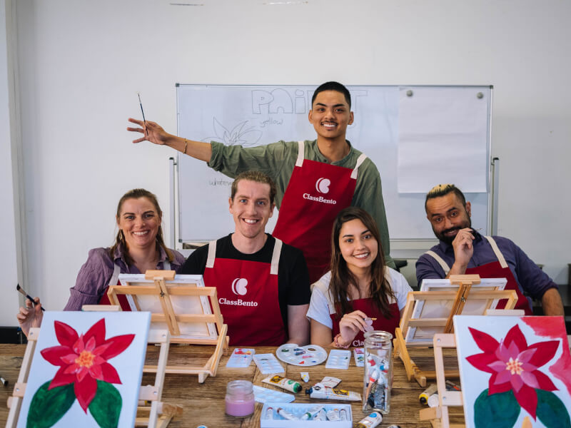 A group of people wearing red aprons posing behind art canvases. 