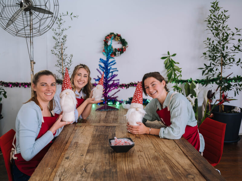 A group of three women holding up DIY Christmas decorations. 