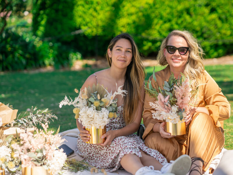 two women posing with dried flower vases