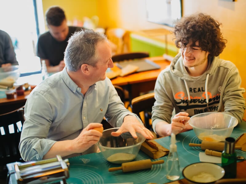 Father's and son smiling at one another at a pasta-making class