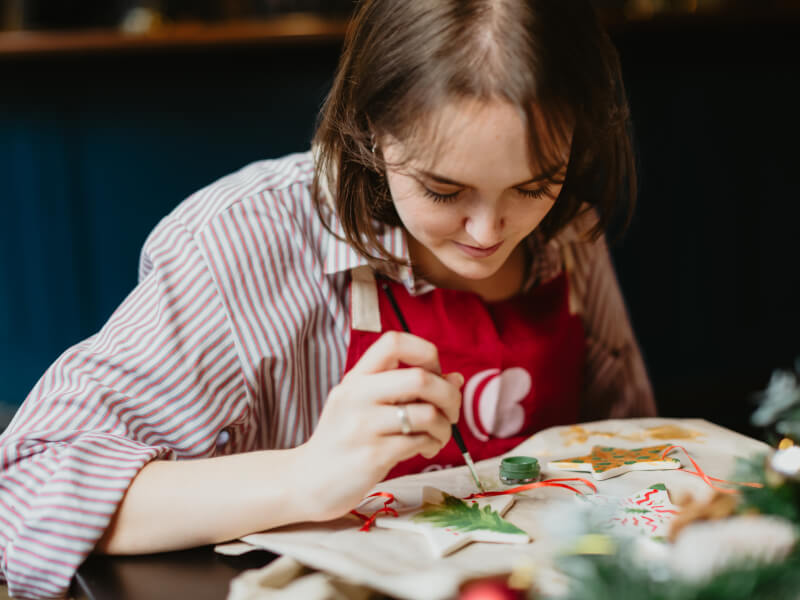Girl in striped shirt painting ceramic Christmas decorations