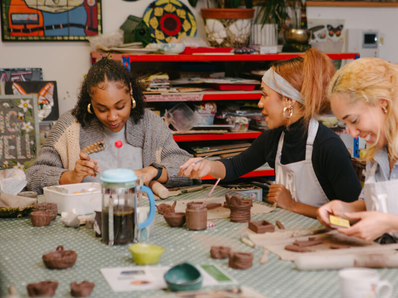 Group of women seated at a workbench making ceramics
