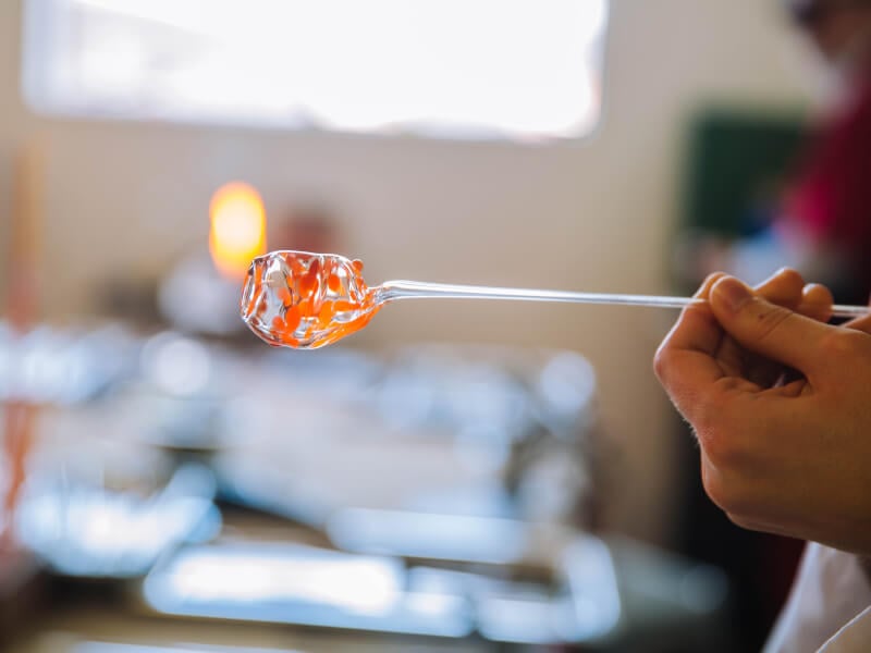 Hand holding a molten glass-blown object on a rod