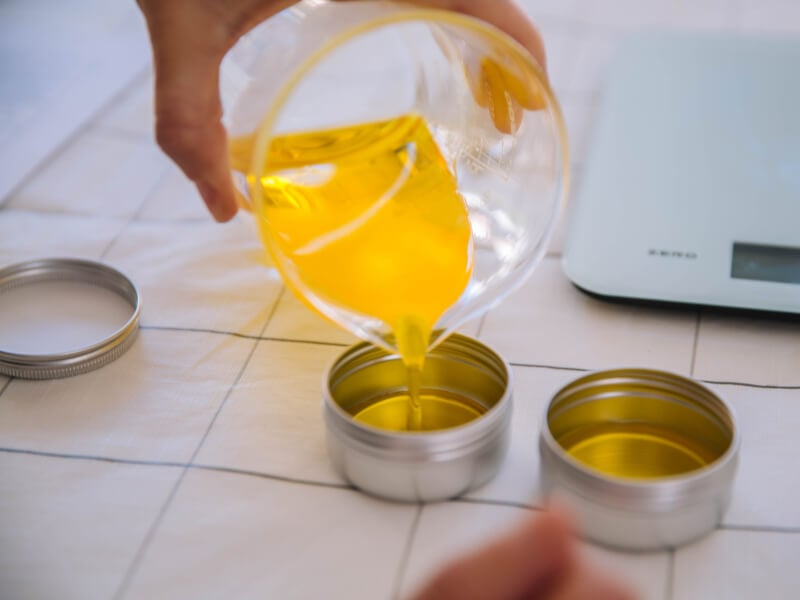 Hand pouring beaker full of oil into two small metal canisters