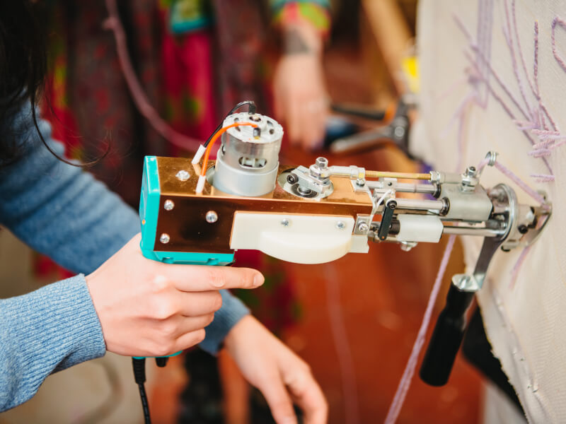Hands holding a tufting gun up to canvas
