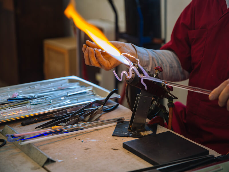 Hands holding blow torch and glass rod