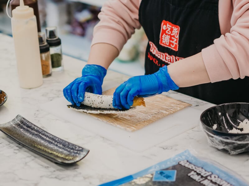 Hands in blue gloves rolling sushi