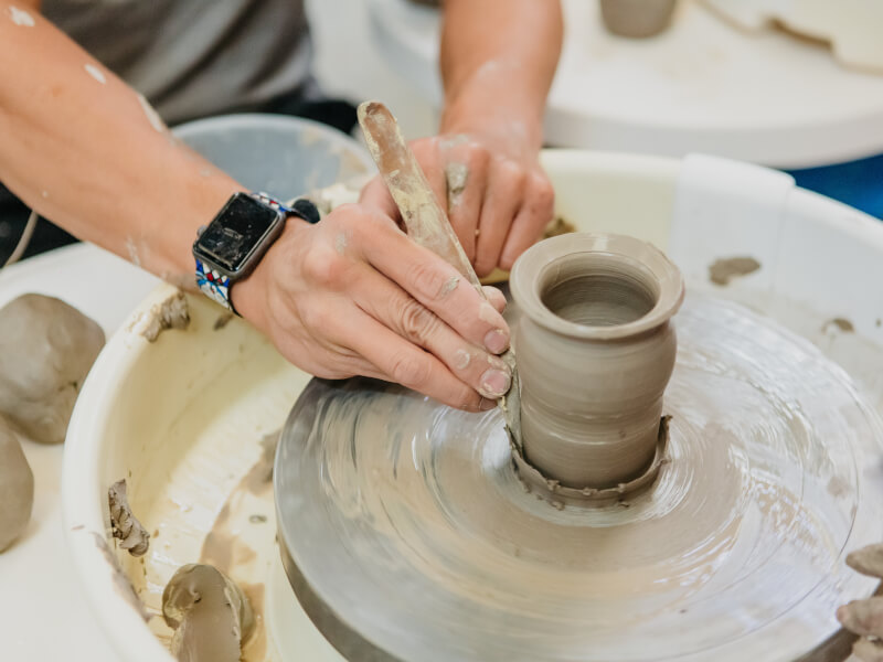 Hands shaping a clay pot on a pottery wheel