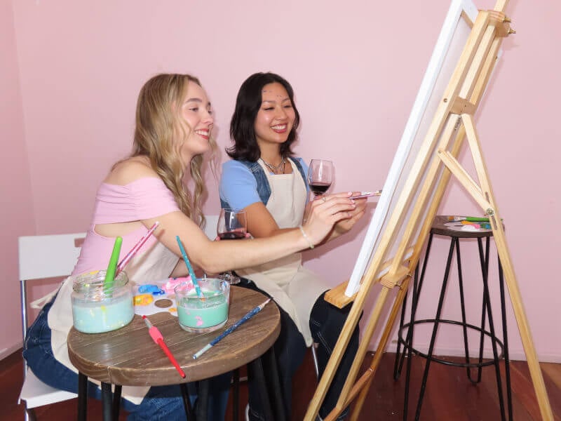 Colleagues painting while holding a glass of wine