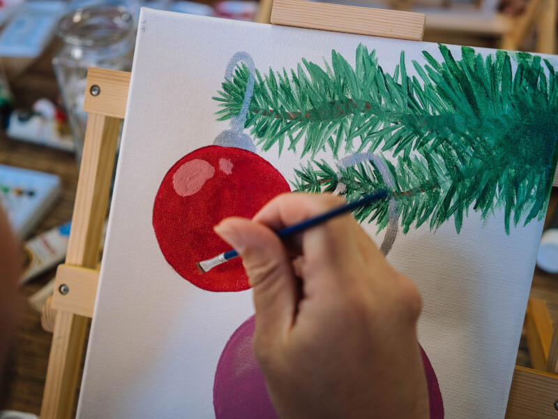 A hand painting a bauble on a Christmas tree