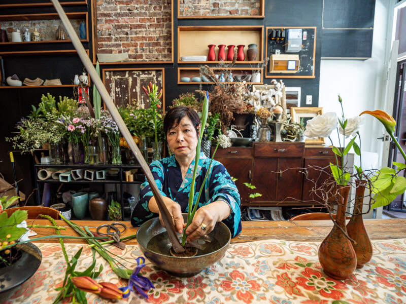 Older woman standing behind ikebana
