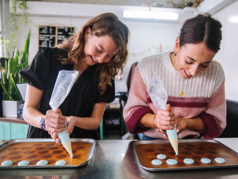 two women smiling and piping macarons at a Perth cooking class
