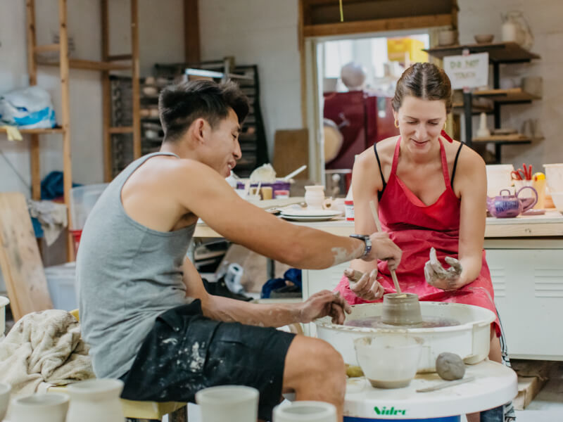 Man and woman sitting at a pottery wheel spinning clay