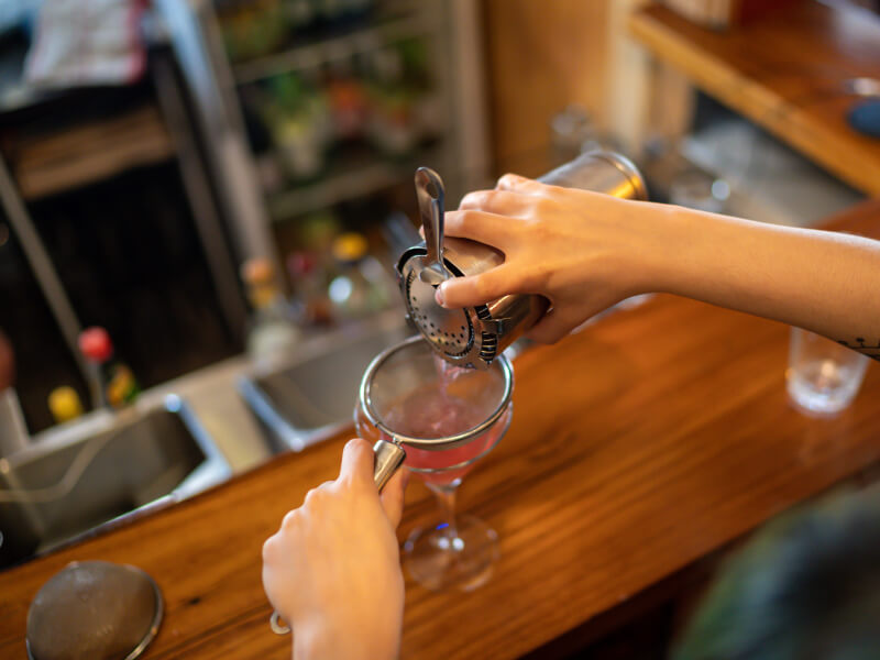 A cocktail student pours their cocktail into a glass
