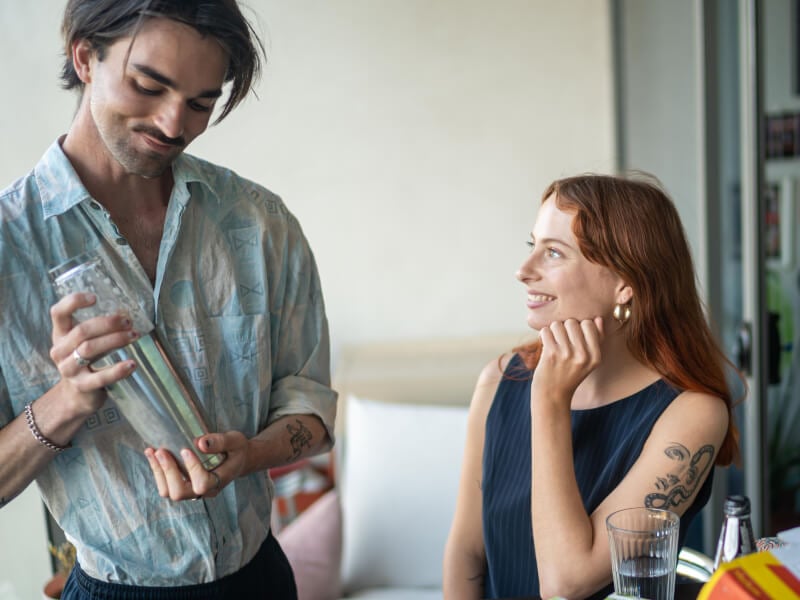 A woman looking at a man shaking up a cocktail