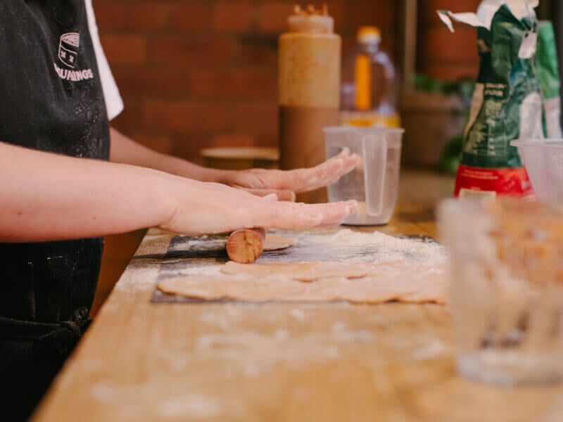 Person rolling out dough on a floured bench