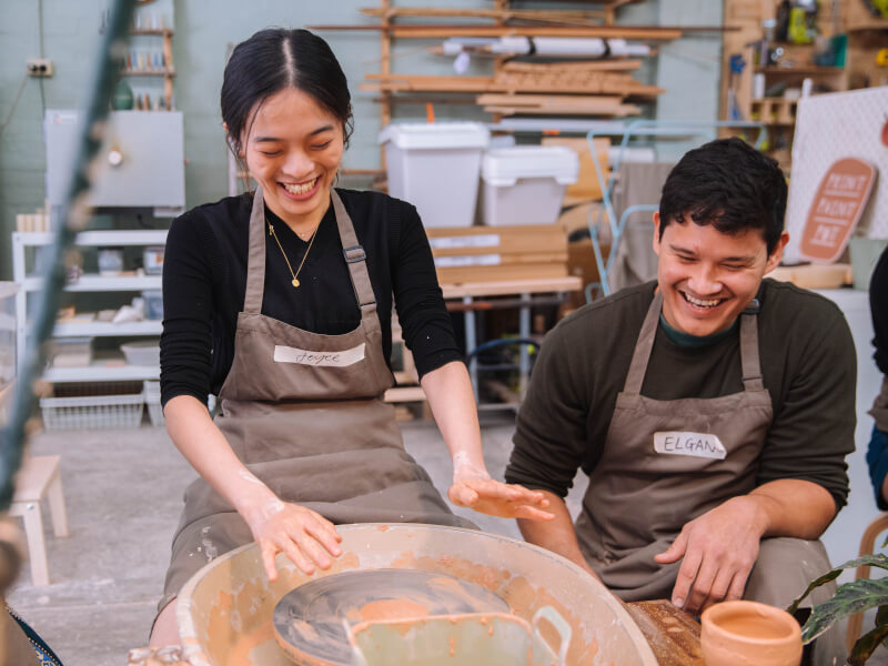 A couple laughing at a wheel throwing class.
