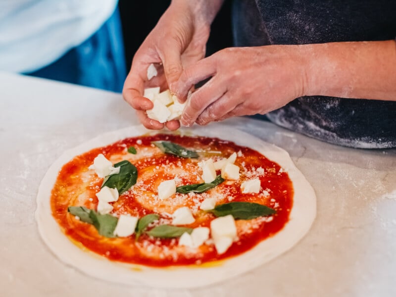 Close-up on hands putting cheese on pizza