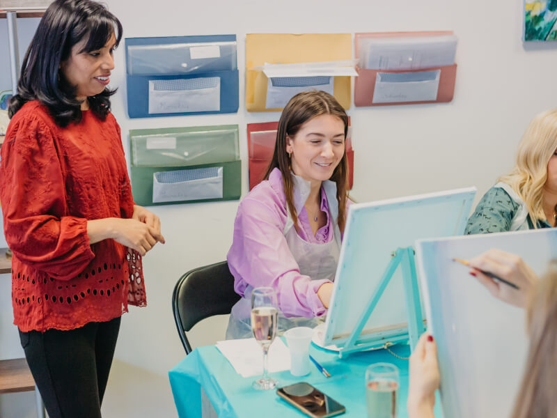 Woman at corporate paint and sip class getting guidance from art instructor