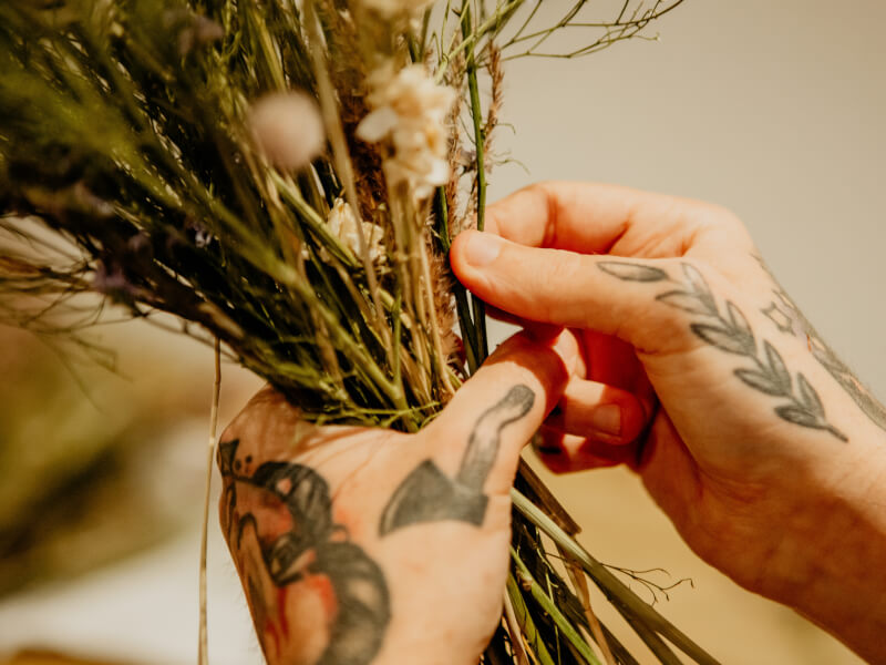 Man's tattooed hands holding a bunch of dried flowers