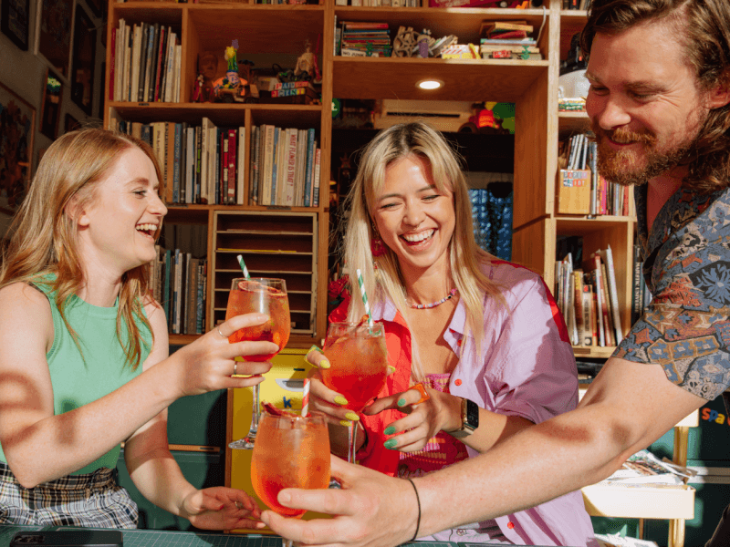 Three smiling people in colourful clothing clinking their glasses