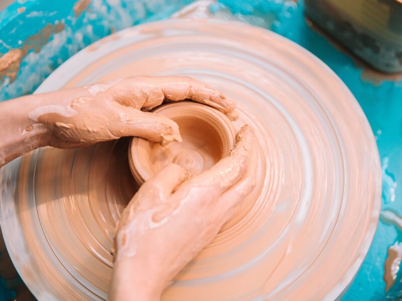 op-down view of hands shaping clay on pottery wheel