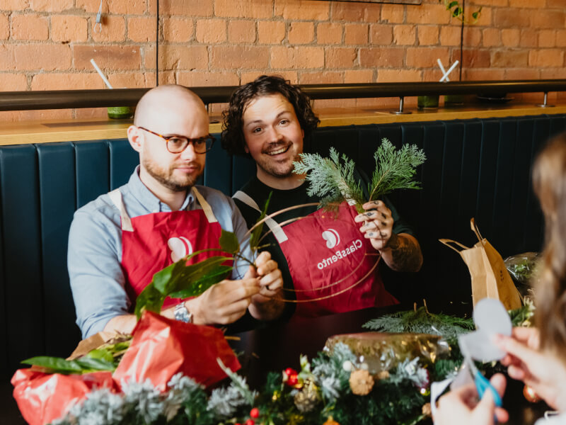 Two men in red aprons making a Christmas wreath