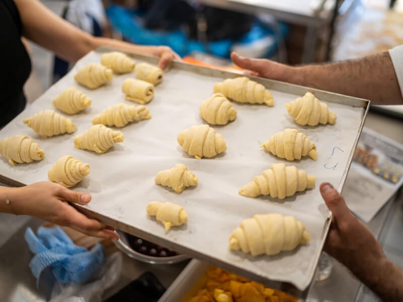 Two people holding a tray of unbaked croissants