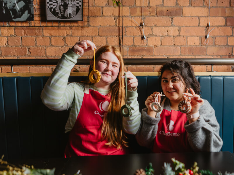 Two smiling women holding up macrame Christmas decorations