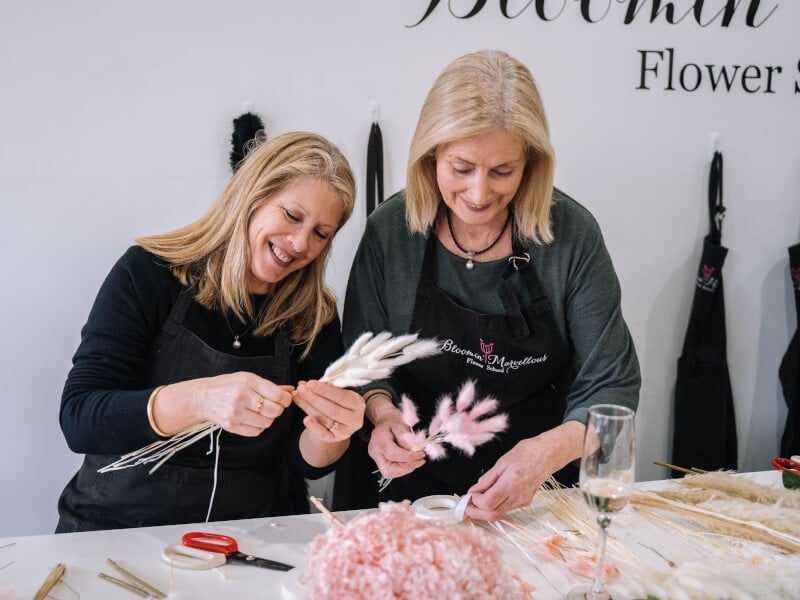 Two smiling women in aprons at a floristry class