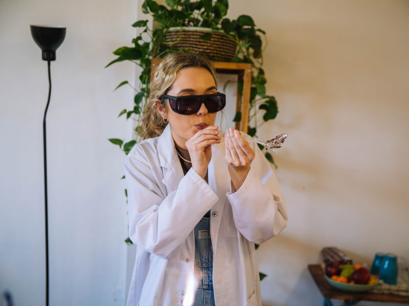 Woman in white coat and dark glasses blowing glass