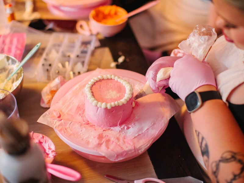 Woman piping white icing onto a pink buttercream cake